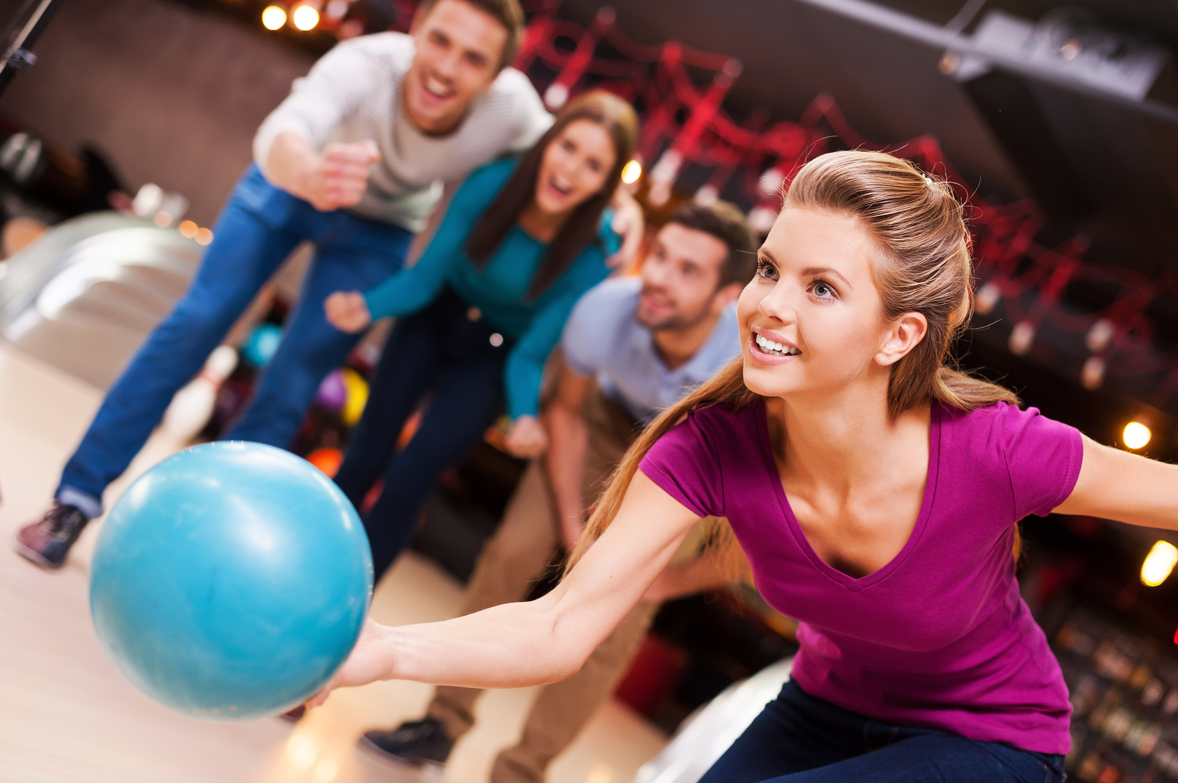 She loves this game. Beautiful young women throwing a bowling ball while three people cheering